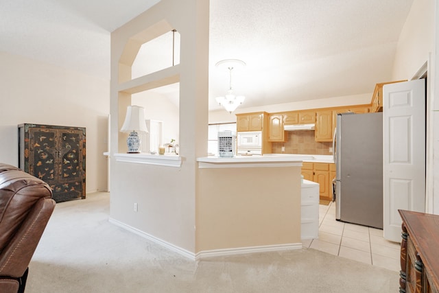 kitchen featuring white microwave, tasteful backsplash, light carpet, stainless steel fridge, and vaulted ceiling