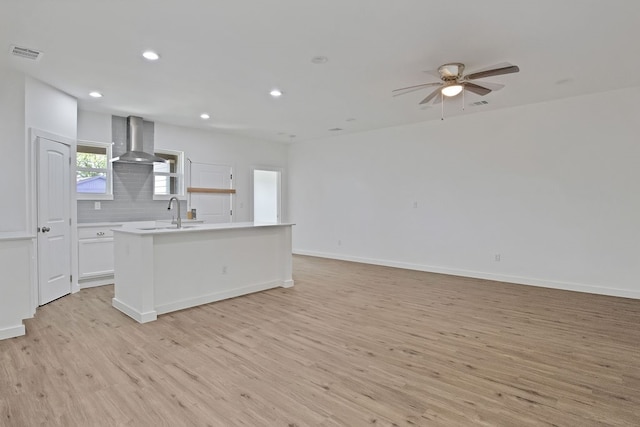 kitchen featuring white cabinetry, wall chimney range hood, a kitchen island, light hardwood / wood-style floors, and decorative backsplash