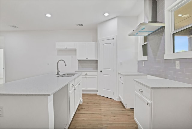 kitchen featuring wall chimney range hood, sink, light hardwood / wood-style floors, decorative backsplash, and white cabinetry