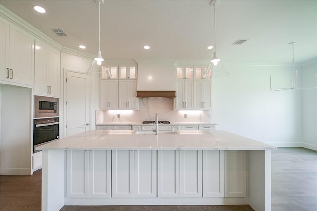 kitchen with white cabinets, an island with sink, built in microwave, and oven