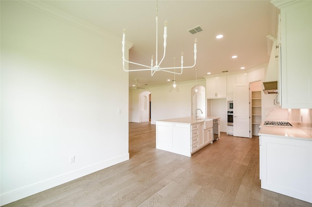 kitchen with ornamental molding, stainless steel appliances, light hardwood / wood-style floors, and a center island with sink