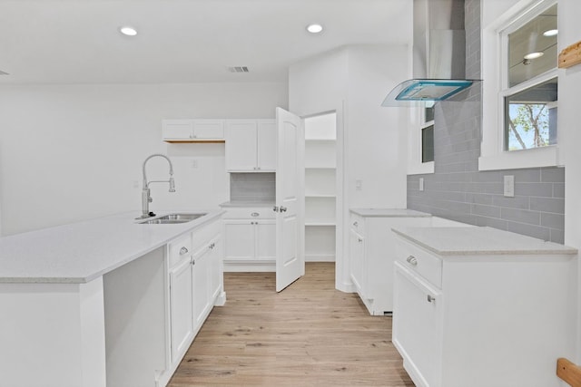 kitchen featuring backsplash, light hardwood / wood-style flooring, sink, and wall chimney range hood