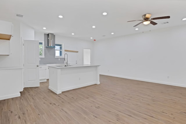 kitchen featuring white cabinets, a center island, light hardwood / wood-style floors, wall chimney exhaust hood, and sink