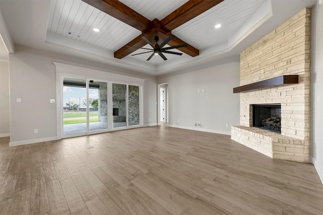 unfurnished living room with wood ceiling, ceiling fan, wood-type flooring, beam ceiling, and a stone fireplace