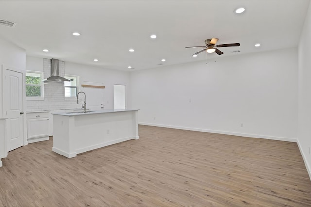 kitchen with light hardwood / wood-style flooring, white cabinets, wall chimney exhaust hood, and tasteful backsplash