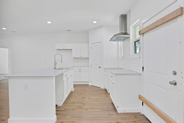 kitchen with tasteful backsplash, wall chimney range hood, white cabinets, sink, and light hardwood / wood-style flooring