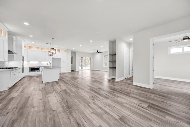 unfurnished living room with a wealth of natural light, ceiling fan with notable chandelier, and light hardwood / wood-style floors