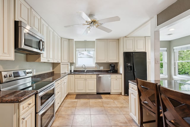 kitchen featuring light tile patterned flooring, dark stone counters, ceiling fan, stainless steel appliances, and sink