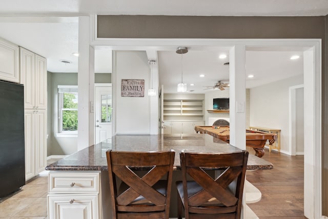 kitchen featuring dark stone counters, black refrigerator, pendant lighting, pool table, and light hardwood / wood-style flooring