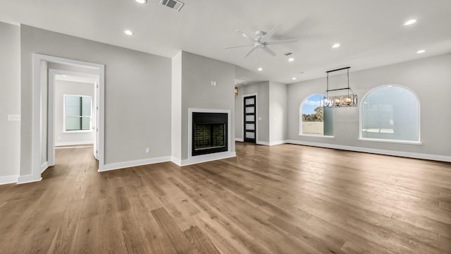 unfurnished living room featuring ceiling fan with notable chandelier and light hardwood / wood-style flooring