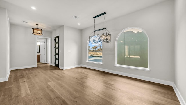 unfurnished dining area featuring an inviting chandelier and wood-type flooring