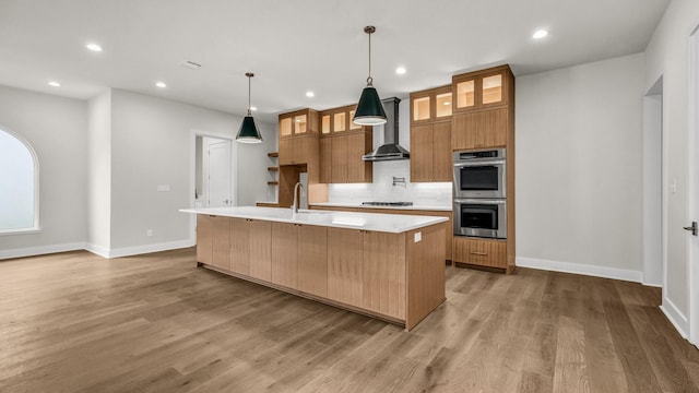 kitchen featuring appliances with stainless steel finishes, pendant lighting, sink, a large island, and wall chimney range hood