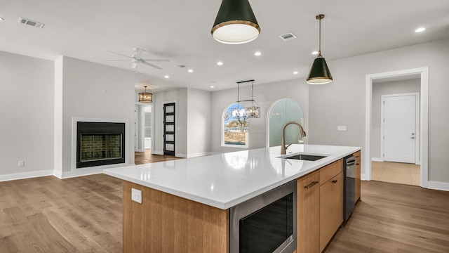 kitchen featuring appliances with stainless steel finishes, decorative light fixtures, an island with sink, sink, and light hardwood / wood-style floors