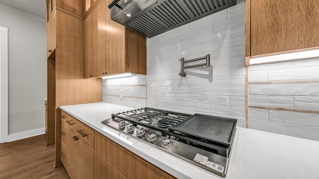 kitchen featuring backsplash, dark wood-type flooring, stainless steel gas cooktop, and wall chimney range hood