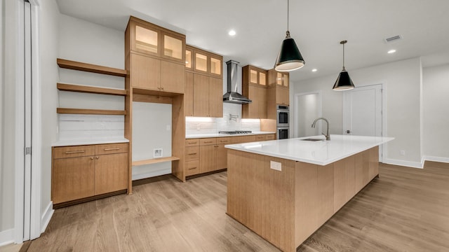 kitchen featuring wall chimney exhaust hood, sink, an island with sink, light hardwood / wood-style floors, and decorative backsplash