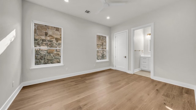 unfurnished bedroom with ceiling fan, ensuite bath, and light wood-type flooring