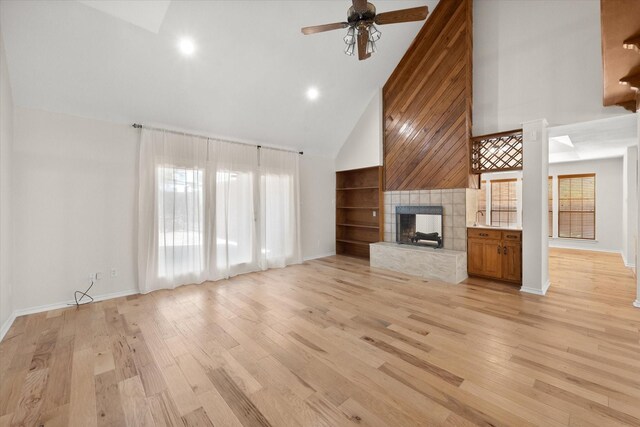 unfurnished living room with high vaulted ceiling, a fireplace, light hardwood / wood-style flooring, and ceiling fan