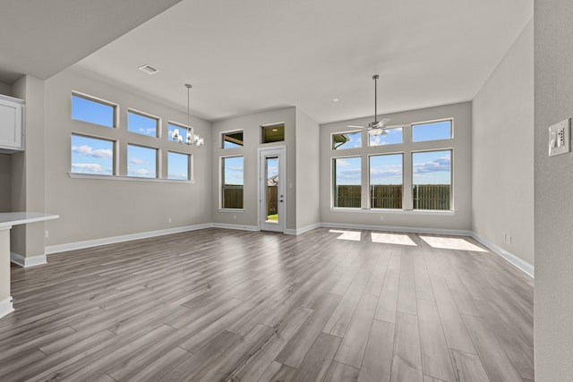 unfurnished living room with ceiling fan with notable chandelier and light hardwood / wood-style floors