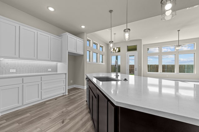 kitchen with sink, hanging light fixtures, a healthy amount of sunlight, light stone countertops, and white cabinets