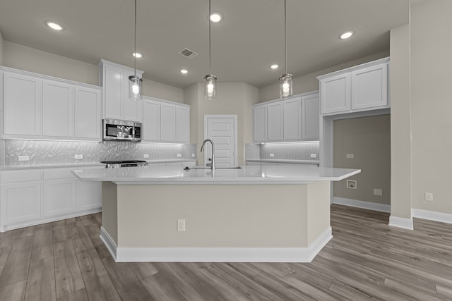 kitchen with decorative light fixtures, a center island with sink, and white cabinets