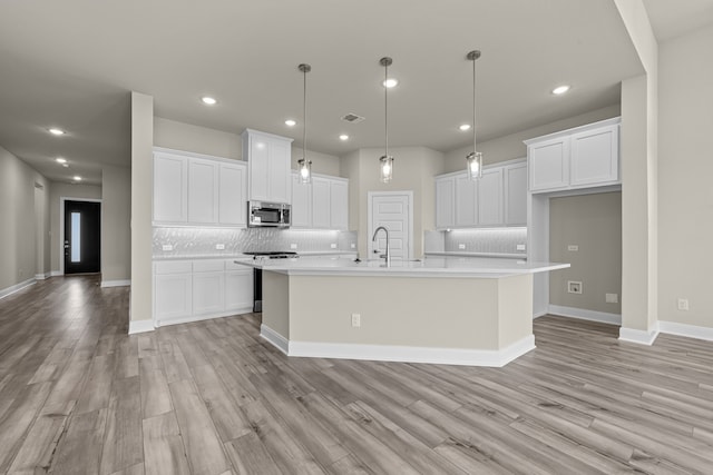 kitchen with pendant lighting, an island with sink, white cabinets, backsplash, and light hardwood / wood-style flooring