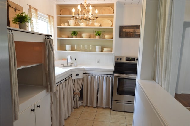 kitchen featuring a notable chandelier, stainless steel electric stove, white cabinets, sink, and light tile patterned floors