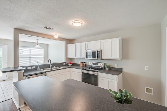 kitchen featuring dark countertops, visible vents, a peninsula, stainless steel appliances, and a sink