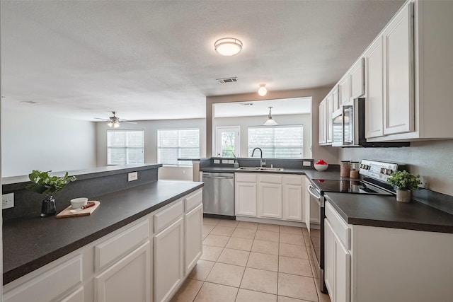 kitchen with a sink, dark countertops, stainless steel appliances, light tile patterned floors, and a healthy amount of sunlight