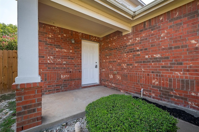 view of exterior entry featuring brick siding and fence