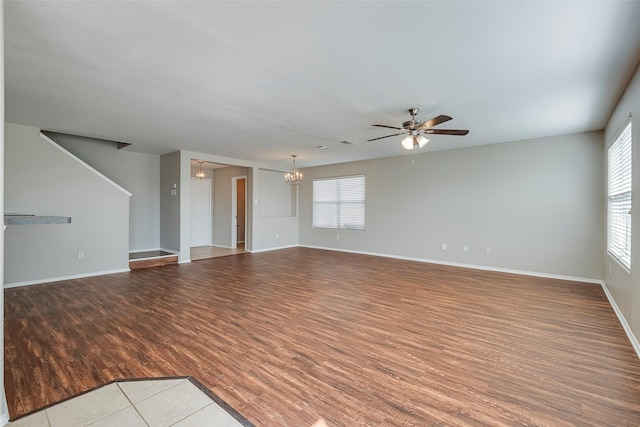 unfurnished living room with ceiling fan with notable chandelier, wood finished floors, and baseboards