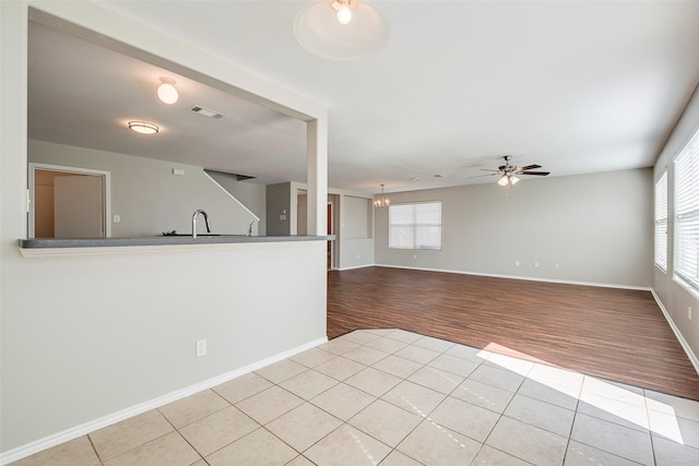 unfurnished living room with visible vents, baseboards, a sink, tile patterned floors, and ceiling fan with notable chandelier