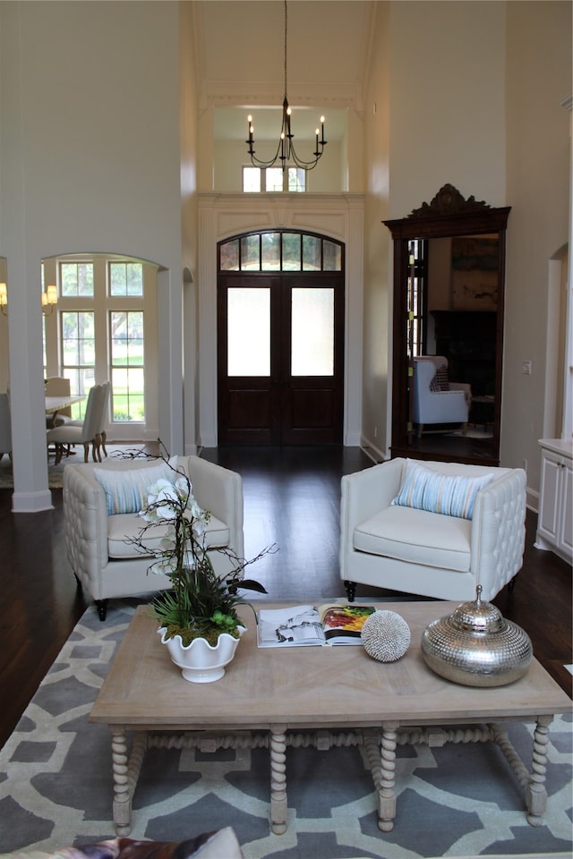 living room with a towering ceiling, dark hardwood / wood-style flooring, decorative columns, and an inviting chandelier