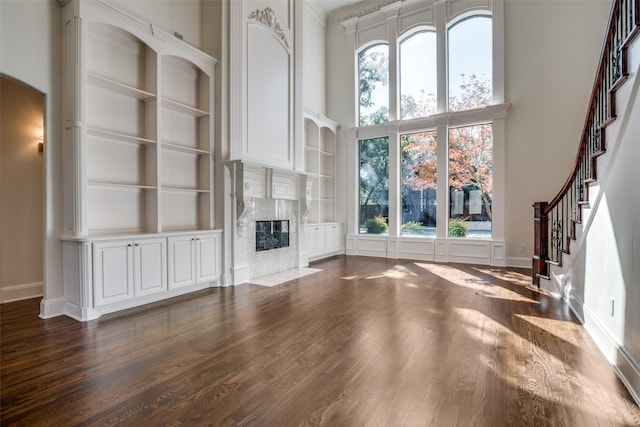 unfurnished living room with built in features, a high ceiling, a fireplace, and wood-type flooring