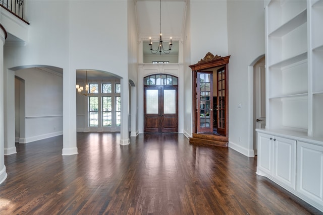 entrance foyer with ornate columns, an inviting chandelier, dark hardwood / wood-style flooring, and a high ceiling