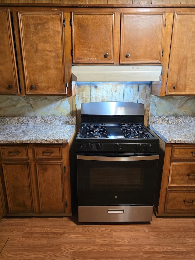 kitchen featuring decorative backsplash, range with gas cooktop, light hardwood / wood-style floors, and light stone counters