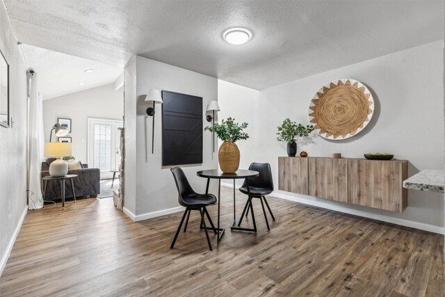 dining space featuring wood-type flooring, vaulted ceiling, and a textured ceiling