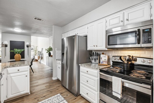 kitchen featuring stainless steel appliances, white cabinets, backsplash, light hardwood / wood-style floors, and light stone countertops