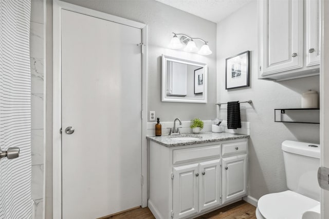 bathroom with wood-type flooring, toilet, vanity, and a textured ceiling