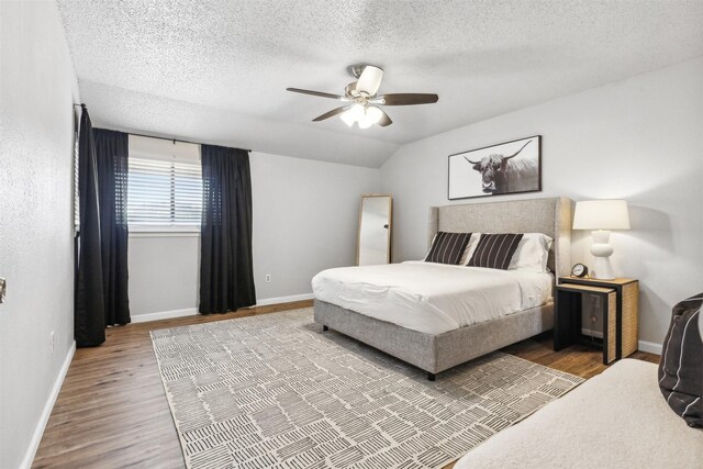 bedroom with vaulted ceiling, a textured ceiling, ceiling fan, and hardwood / wood-style floors