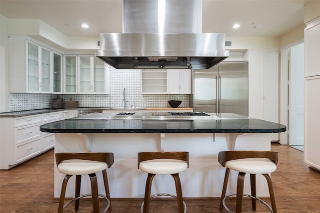 kitchen with tasteful backsplash, a kitchen island, stainless steel appliances, island exhaust hood, and hardwood / wood-style flooring