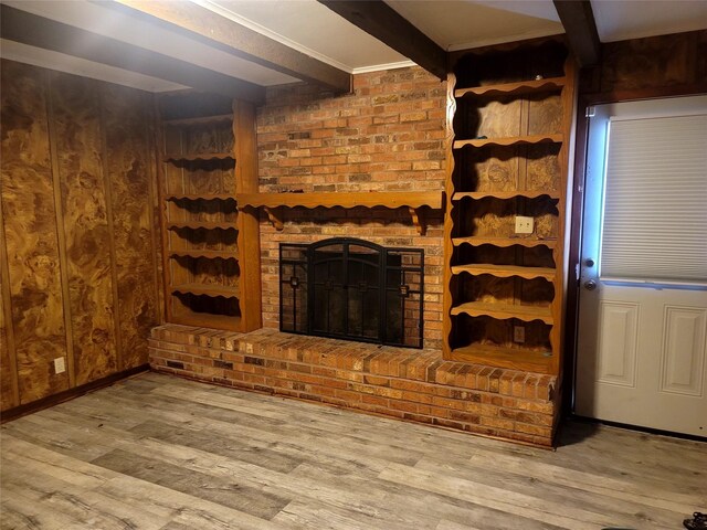 unfurnished living room with a brick fireplace, beamed ceiling, wooden walls, and wood finished floors