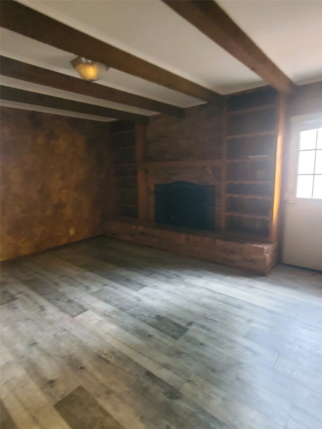 unfurnished living room with beam ceiling, wood finished floors, and a fireplace