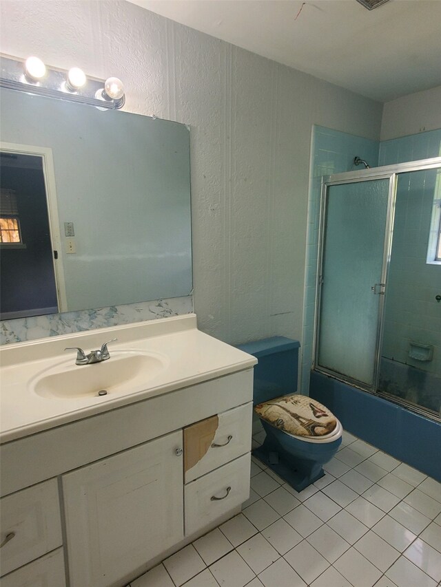 bathroom featuring toilet, a textured wall, tile patterned floors, combined bath / shower with glass door, and vanity