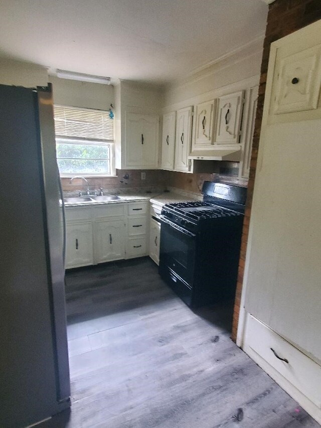 kitchen featuring a sink, under cabinet range hood, freestanding refrigerator, black gas stove, and white cabinets