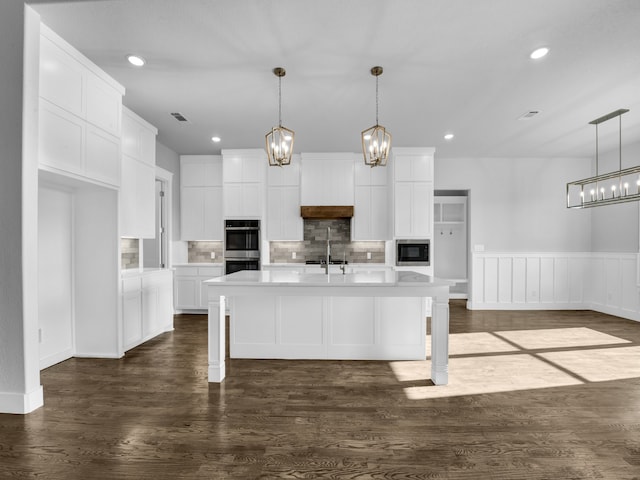 kitchen with double oven, pendant lighting, a center island with sink, dark hardwood / wood-style floors, and white cabinetry