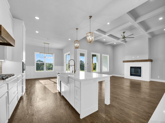 kitchen with beam ceiling, coffered ceiling, a brick fireplace, pendant lighting, and a center island with sink