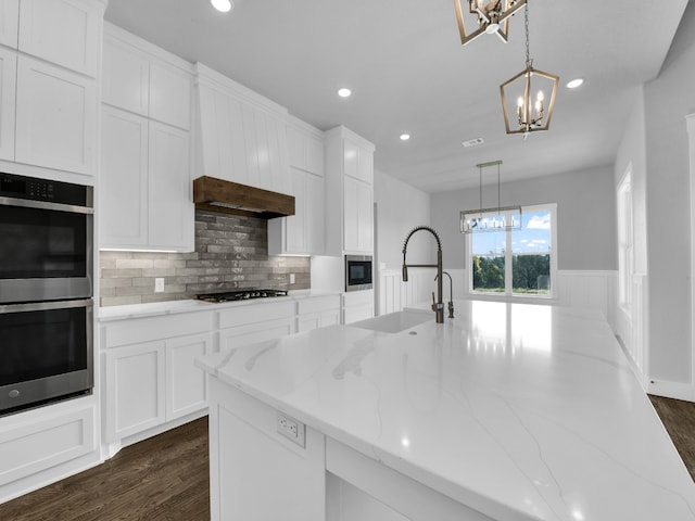 kitchen featuring white cabinetry, sink, light stone countertops, double oven, and decorative light fixtures