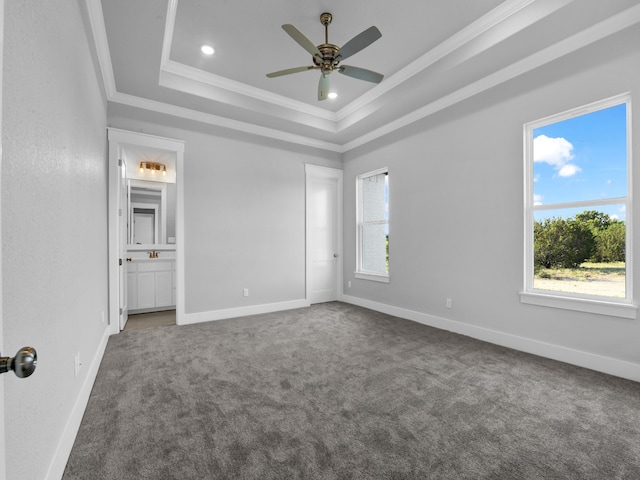 unfurnished bedroom with ensuite bath, a raised ceiling, ceiling fan, crown molding, and multiple windows