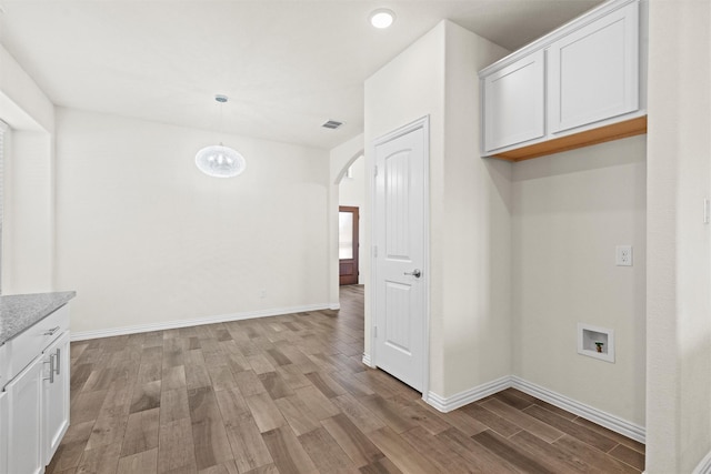 unfurnished dining area featuring arched walkways, light wood finished floors, visible vents, and baseboards