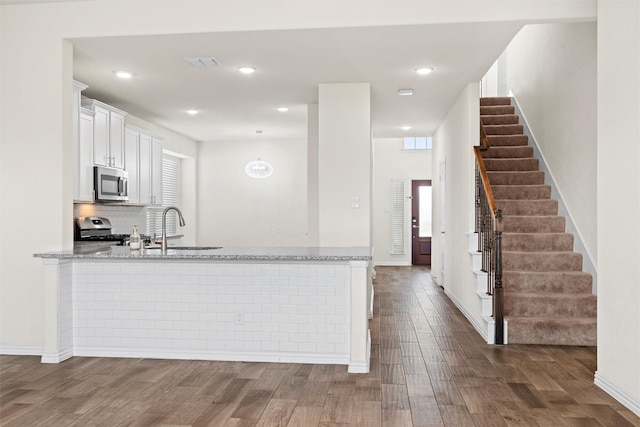 kitchen featuring light stone counters, stainless steel appliances, a peninsula, a sink, and white cabinets